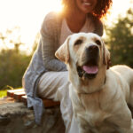 Petland picture of African American mom with Labrador Retriever dog sitting with a field inn the background.