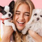 Petland Pembroke Pines picture of a cheerful girl holding a cute Chihuahua puppy and Maltese puppy with a pink background.